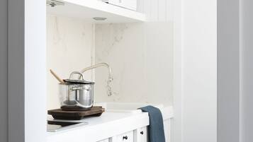 A kitchen with white cabinetry, a microwave, a pot on a wooden board, and a blue towel hanging on the door.