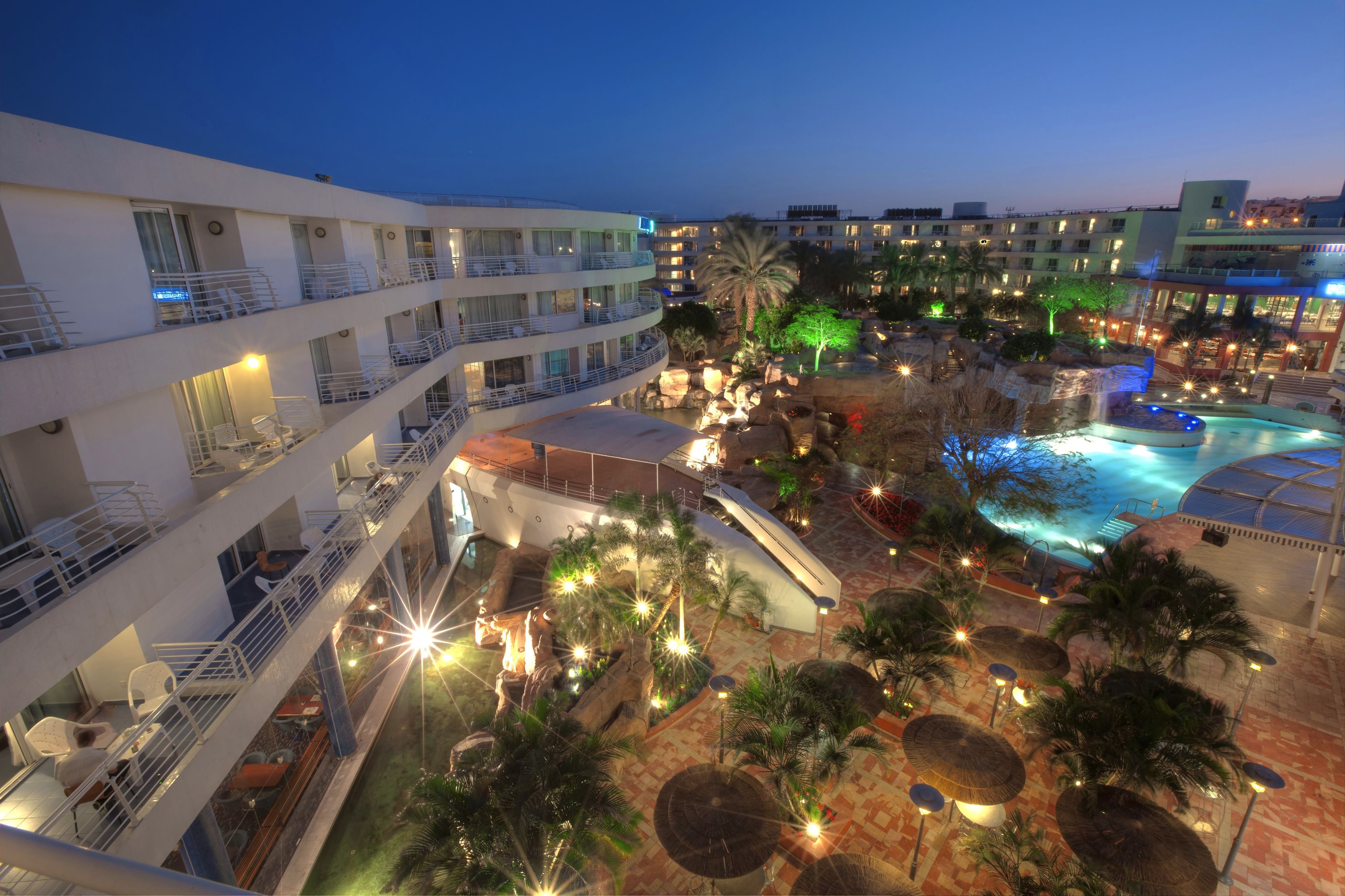 A hotel with multiple balconies, a pool area, and outdoor lighting.