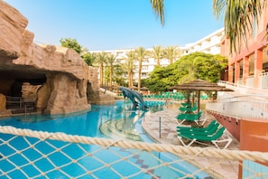 A swimming pool with a rock formation and a water slide, surrounded by lounge chairs and palm trees. - Club Hotel Eilat (Eilat)