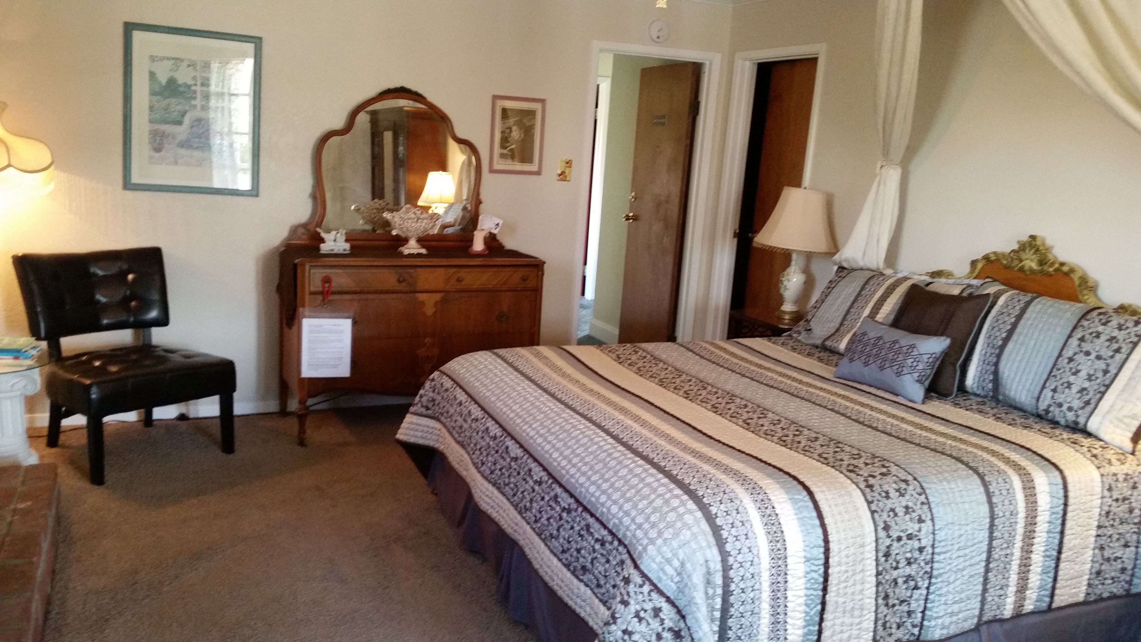 Une chambre à coucher avec un lit, une chaise, une commode, un miroir et une porte.