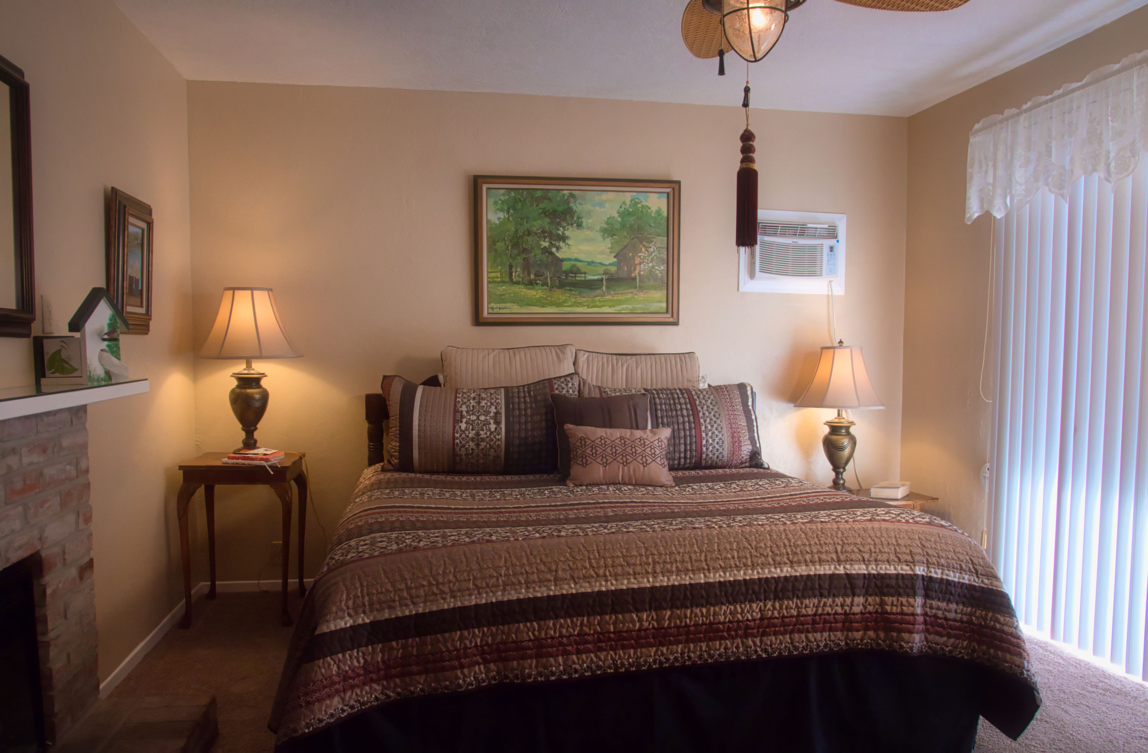 A bedroom with a large bed, two bedside tables with lamps, a painting on the wall, and a window with curtains.