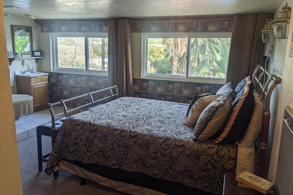 A bedroom with a large bed, a bedside table, a mirror, and a window with curtains.