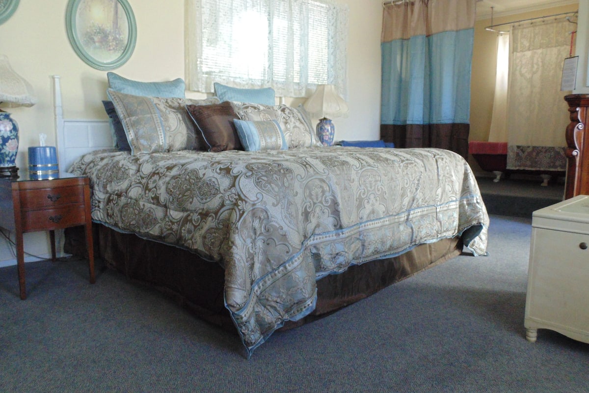 A bedroom with a large bed, a nightstand, a dresser, and a window with curtains.