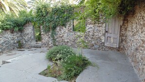 A stone-walled courtyard with a small garden area, a wooden door, and a stone wall with a window. - The Parks Inn Bed and Breakfast (Lemon Cove)