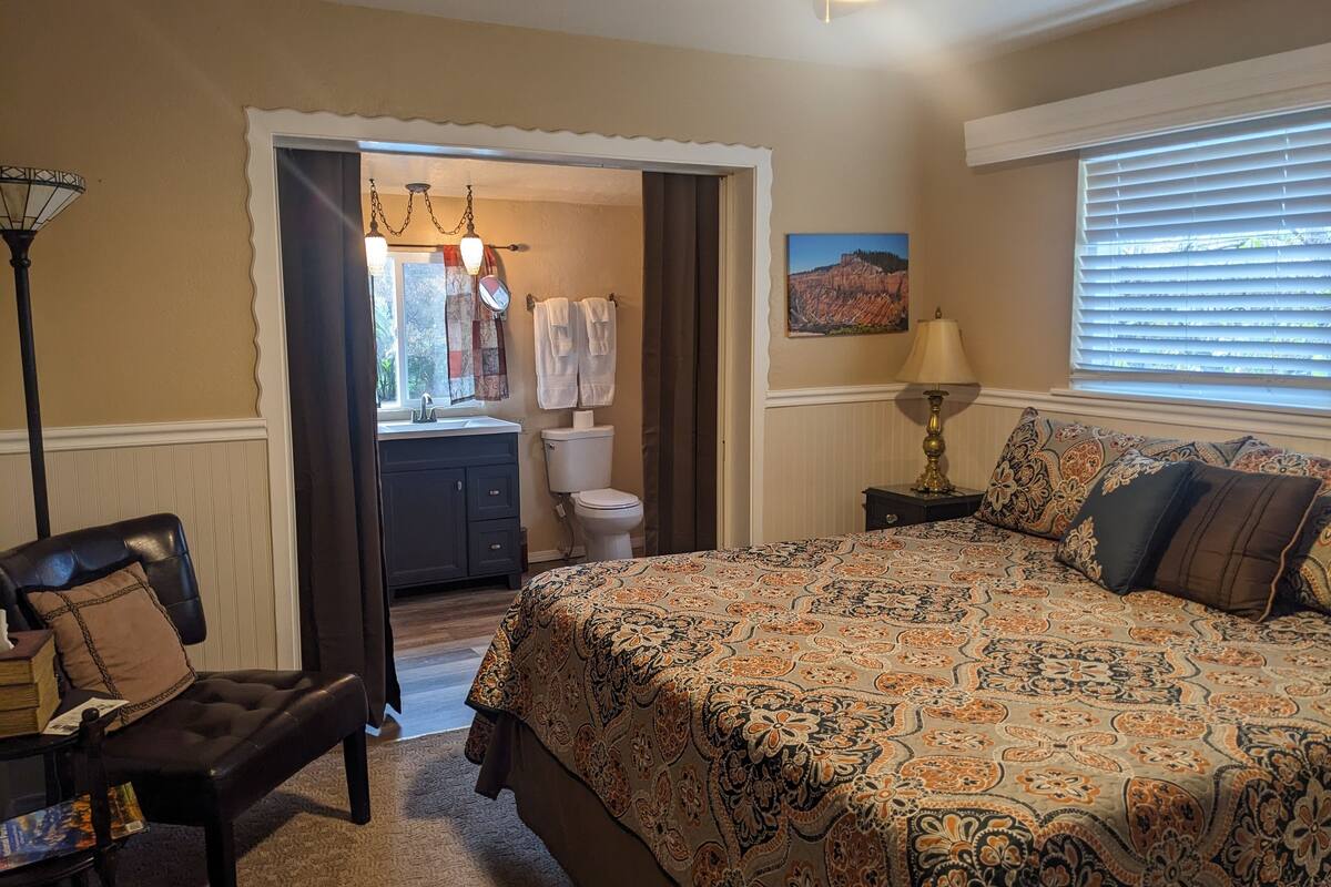 A bedroom with a large bed, a dresser, a chair, a lamp, and a window with blinds.
