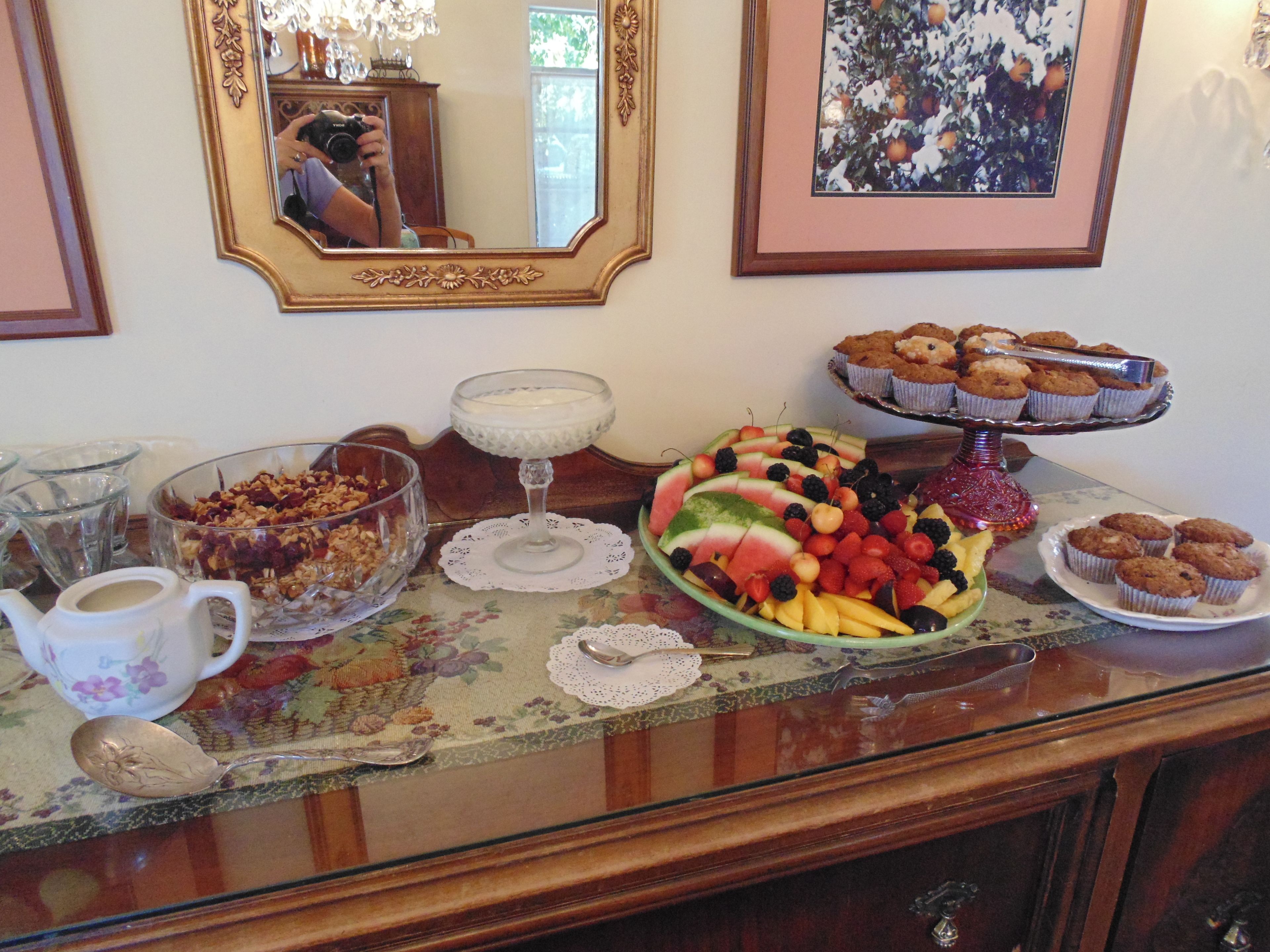 Uma mesa de buffet com diversos alimentos, um espelho e um quadro pendurado na parede.