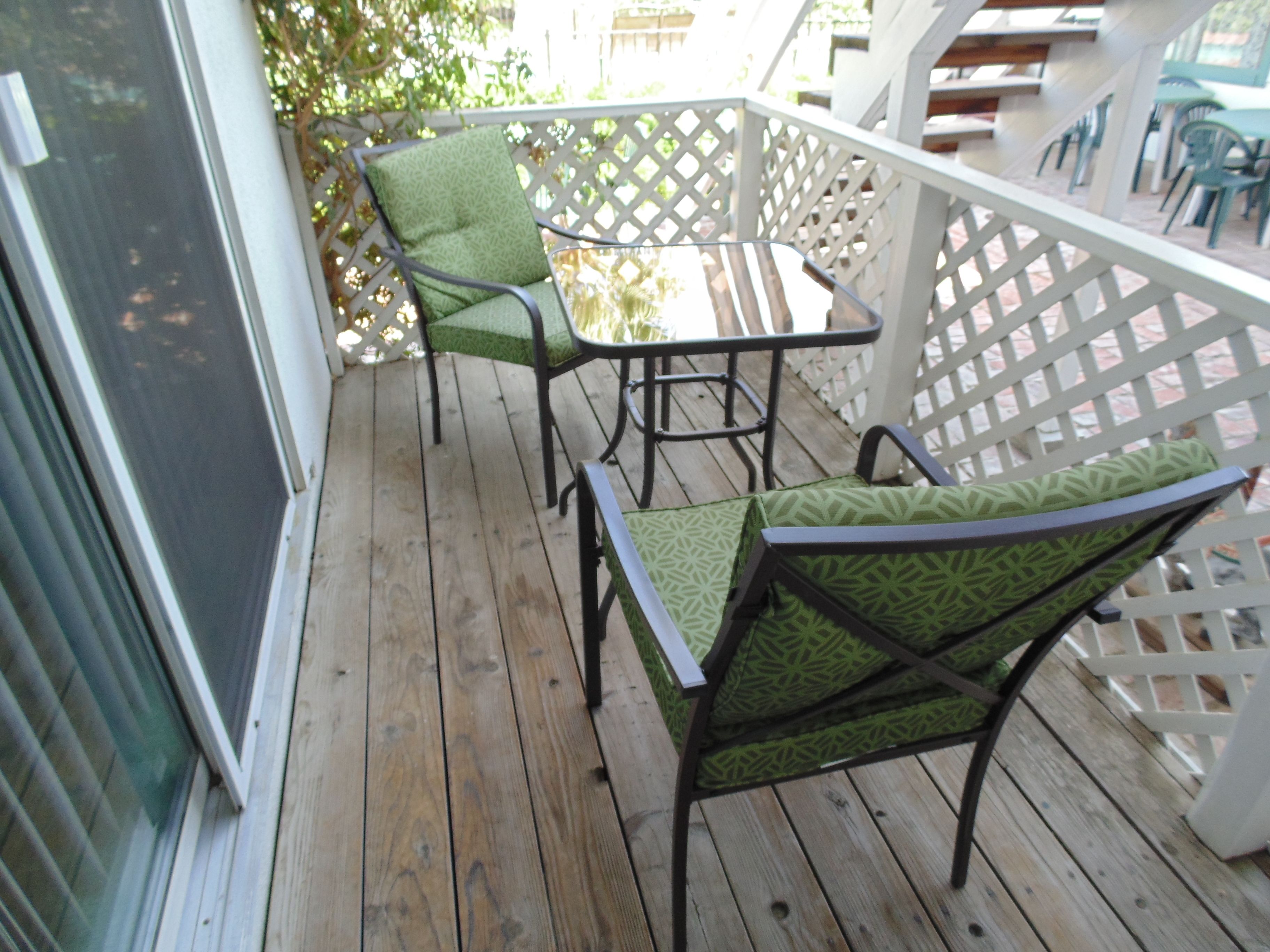 A wooden deck with two green patterned chairs and a small table.
