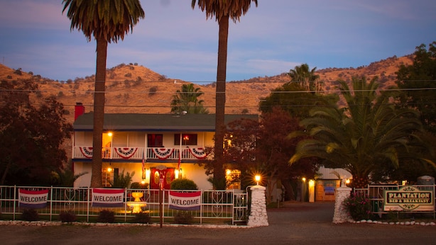 A two-story building with a welcoming sign, palm trees, and a sign for a plantation bed and breakfast. - The Parks Inn Bed and Breakfast (Lemon Cove)