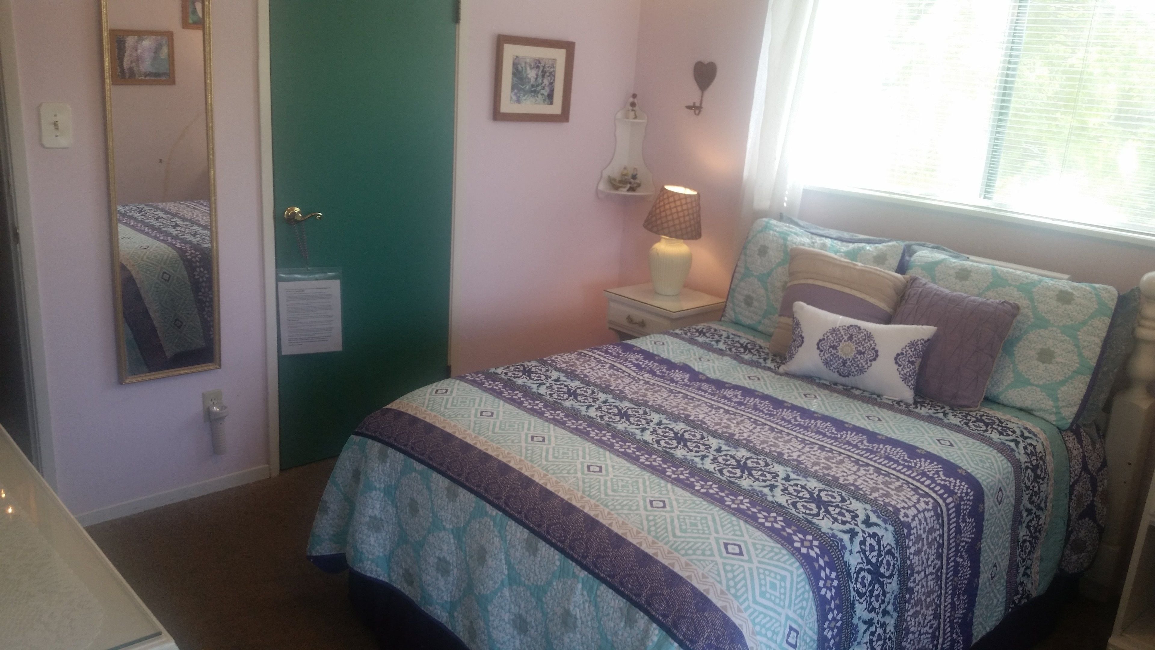 A bedroom with a bed, a nightstand, a lamp, a mirror, and a door.
