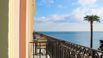 Un balcón con vista al mar, una palmera y un edificio de fachada rosa.