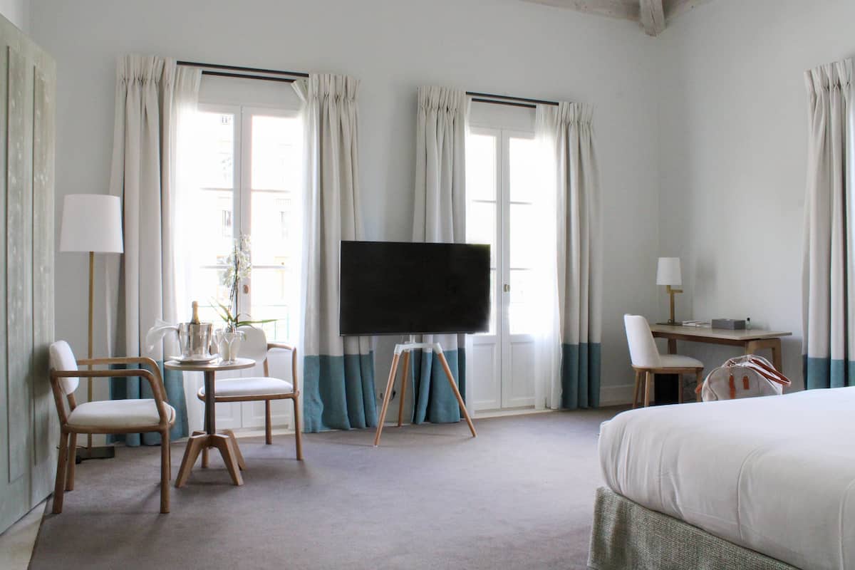 A hotel room with a bed, a desk, a chair, a television on a stand, and curtains on the windows.