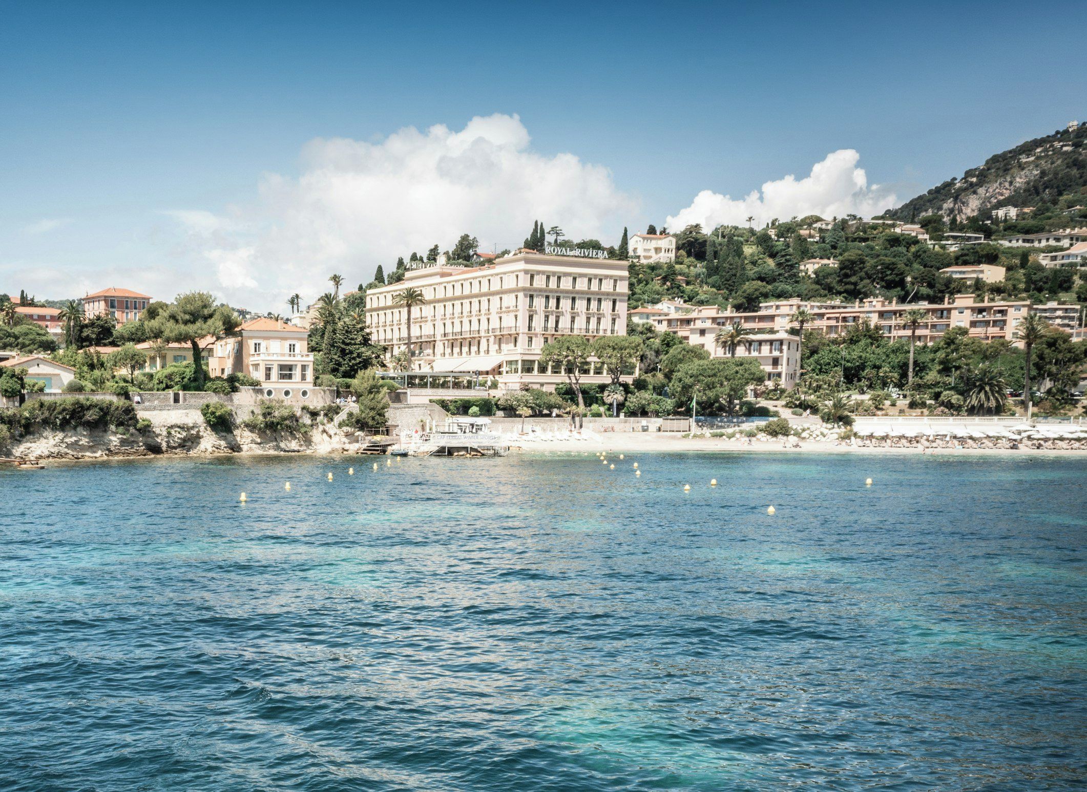 A coastal hotel with a large building, a beach, and a rocky shoreline.