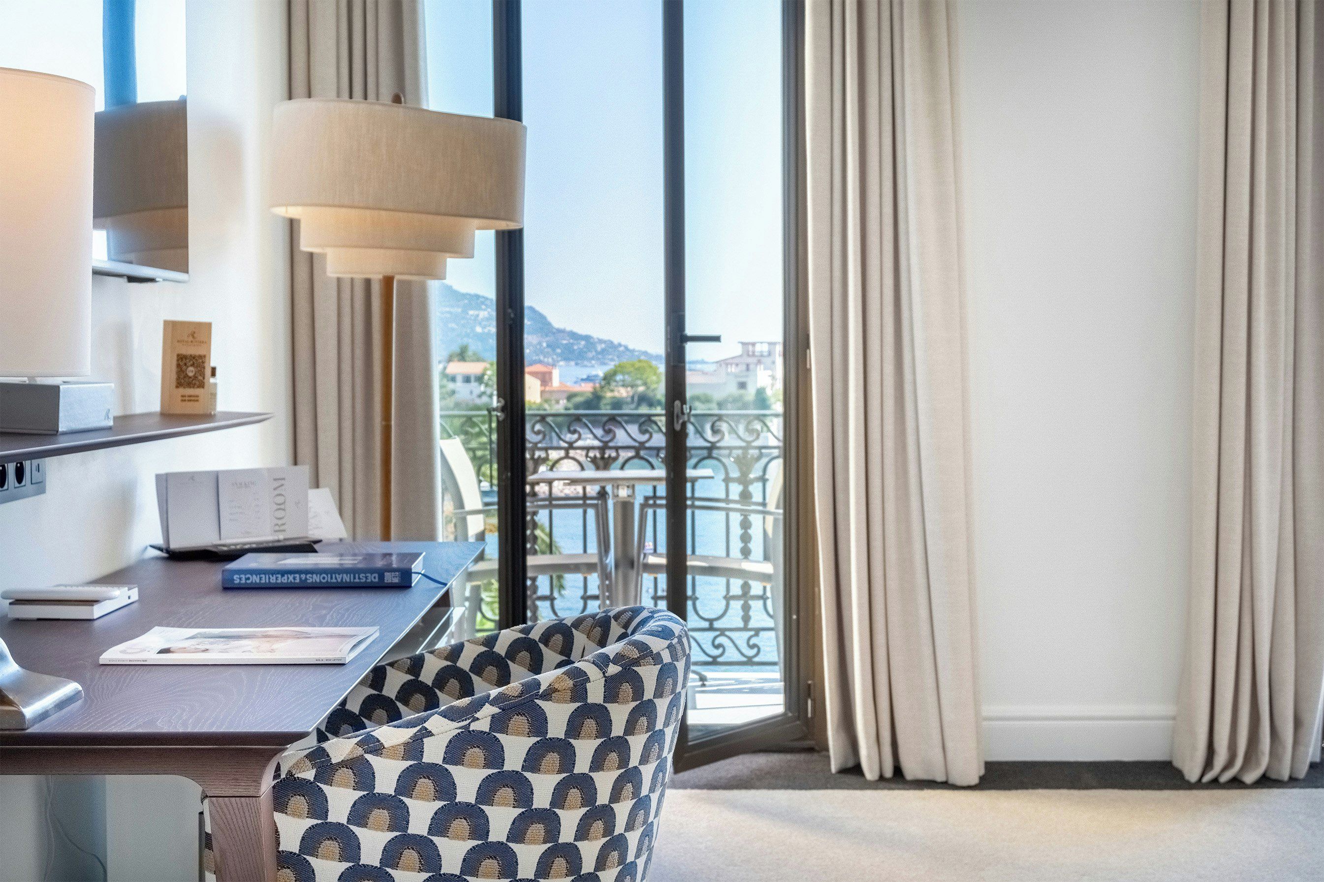 A hotel room with a desk, chair, and a view of the sea through large windows.