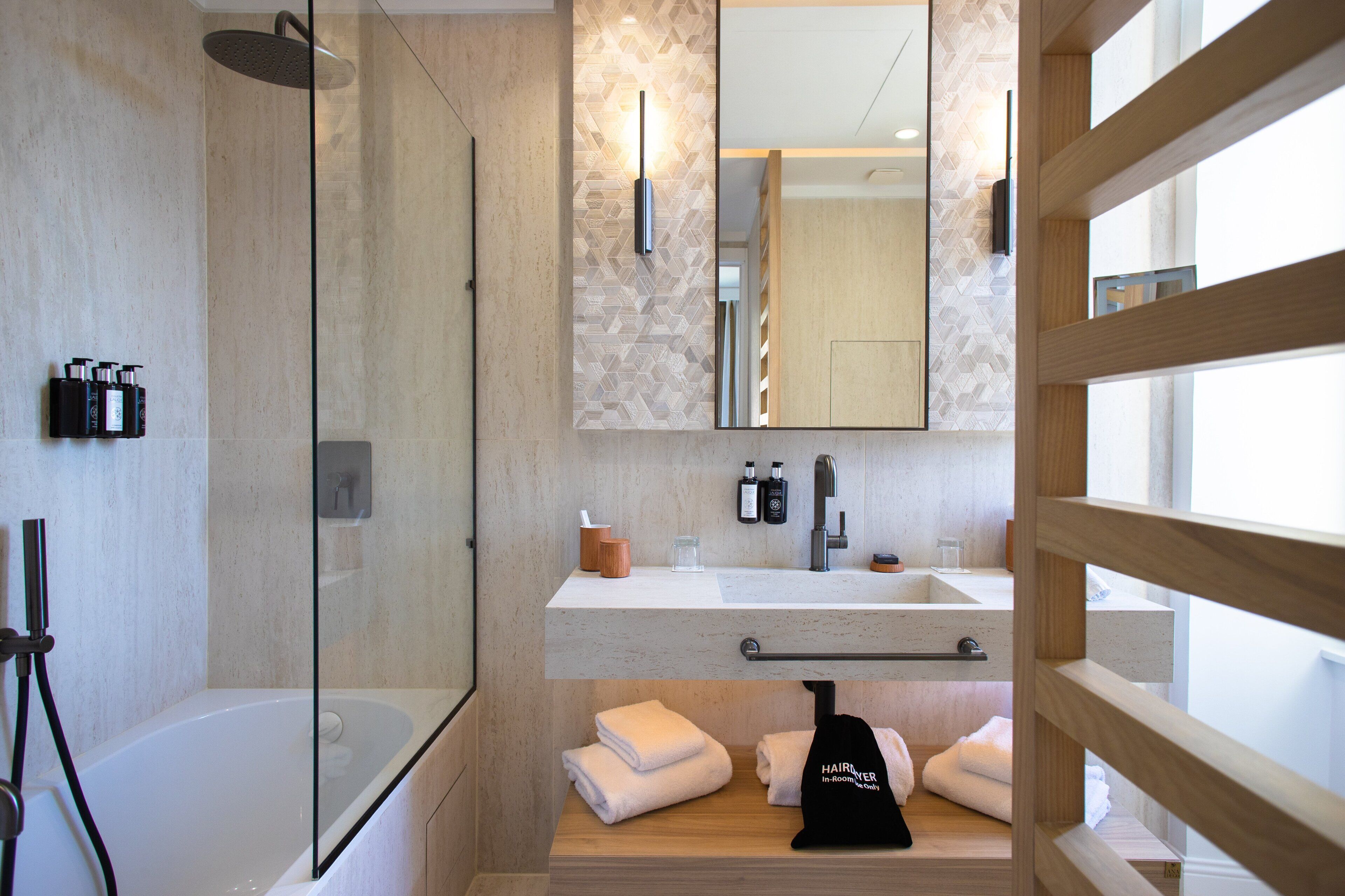 Une salle de bain moderne avec une douche à parois de verre, un grand miroir et un meuble-lavabo en bois doté d’un évier et d’un porte-serviettes.