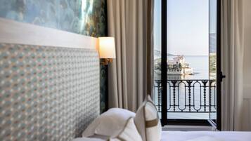 Una camera d'albergo con un letto grande, un quadro appeso al muro e vista mare da un balcone.