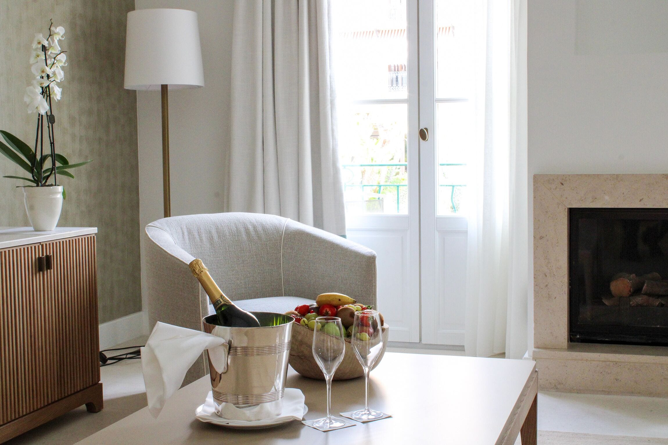 A living room with a sofa, a table with a champagne bottle, glasses, and a fruit bowl.