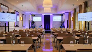 A conference room with tables, chairs, and presentation screens displaying the logo of Royal Riviera.