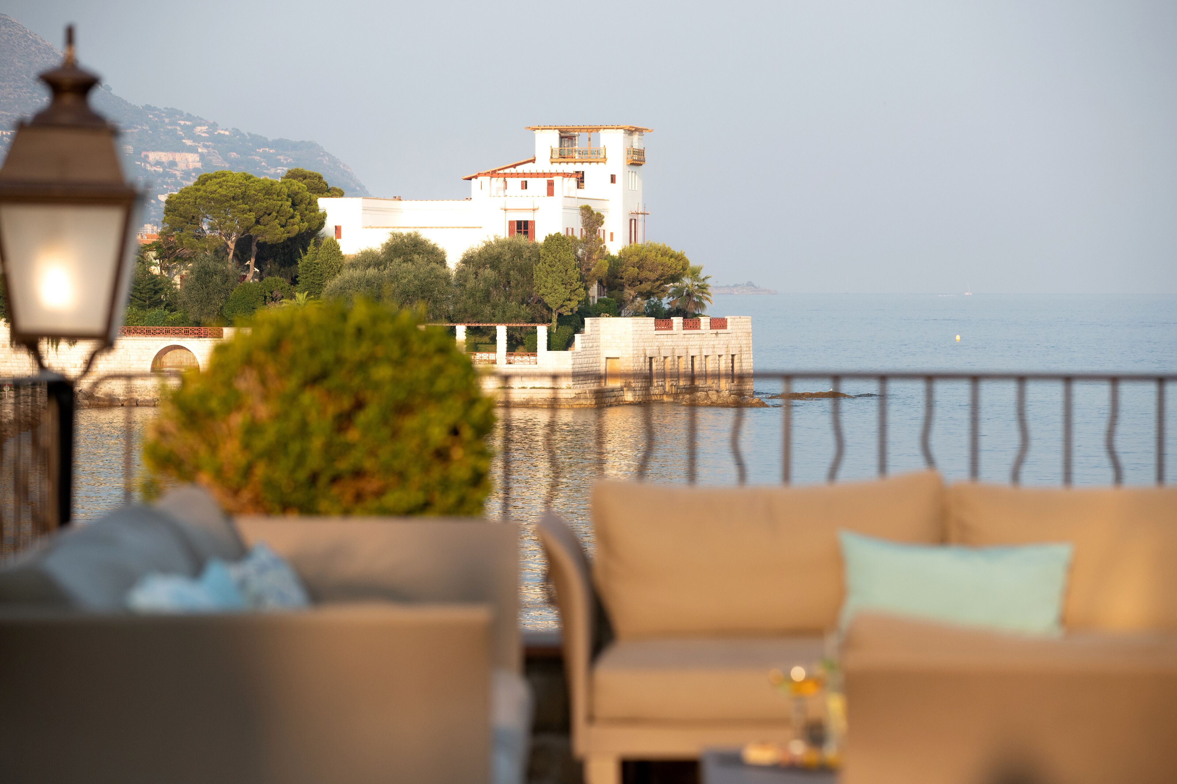 A coastal view with a white building, a balcony, and a dining area with a table and chairs.