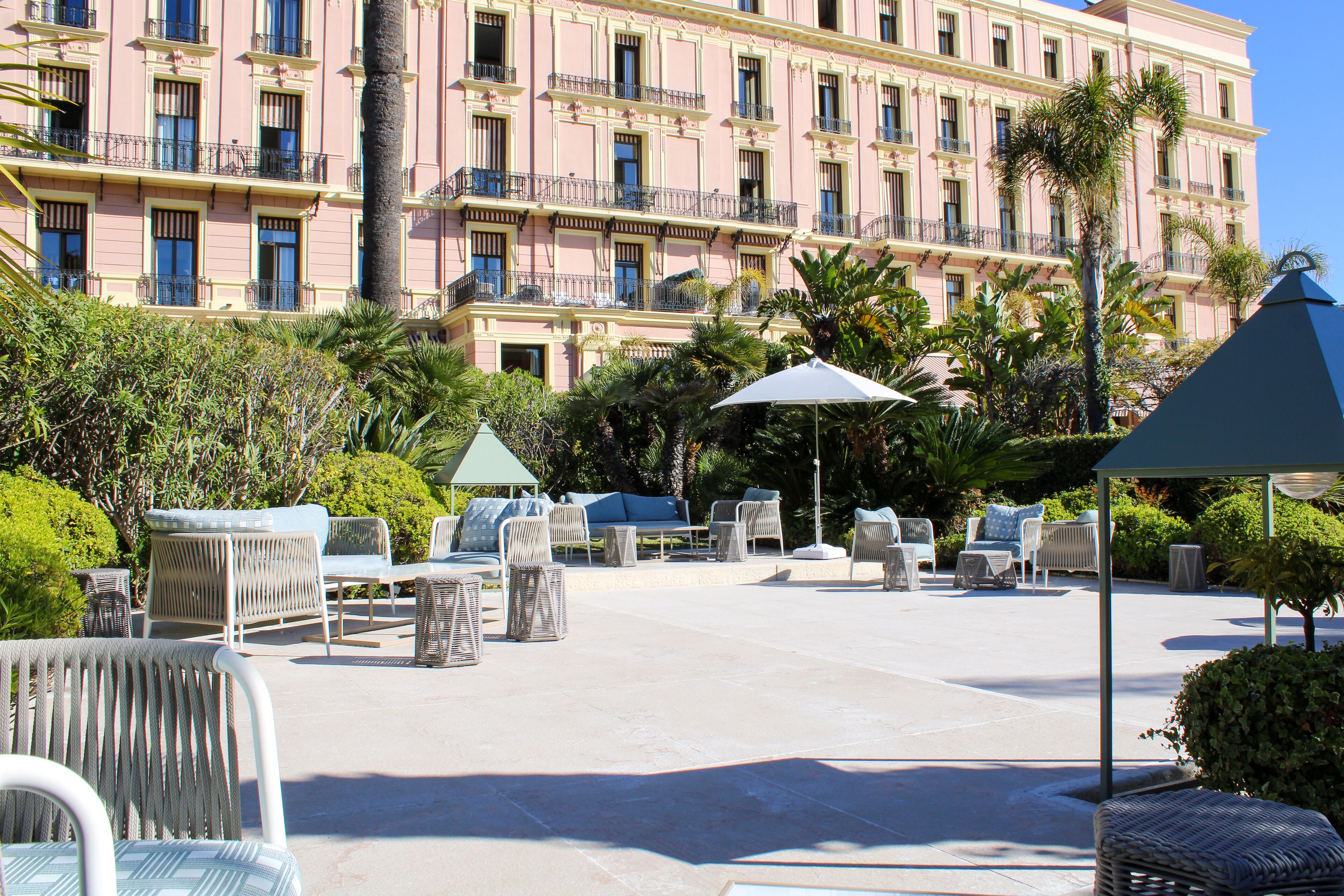 A hotel with outdoor seating, palm trees, and a large building in the background.