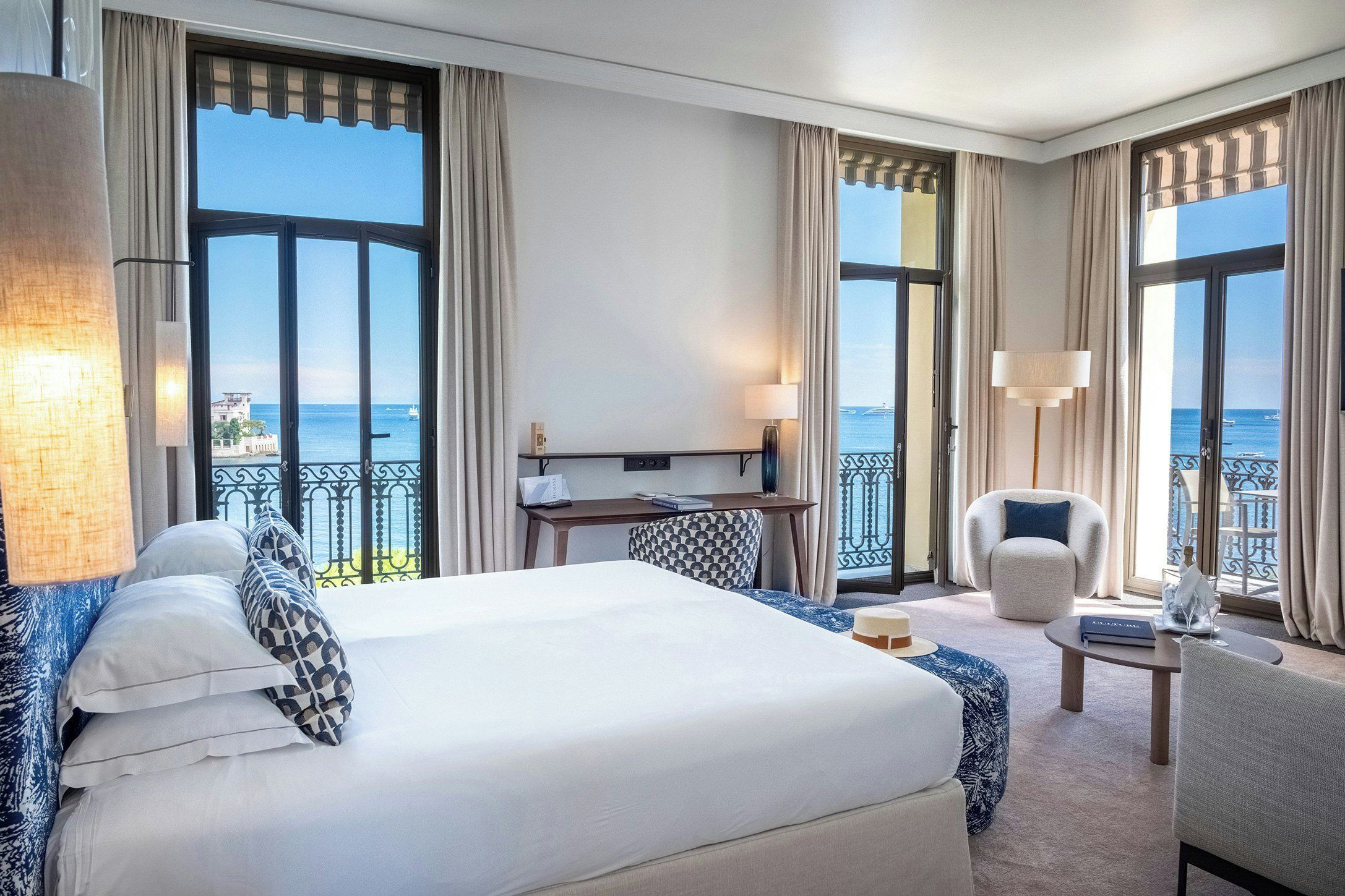 A hotel room with a large bed, a desk, a chair, and a view of the sea.