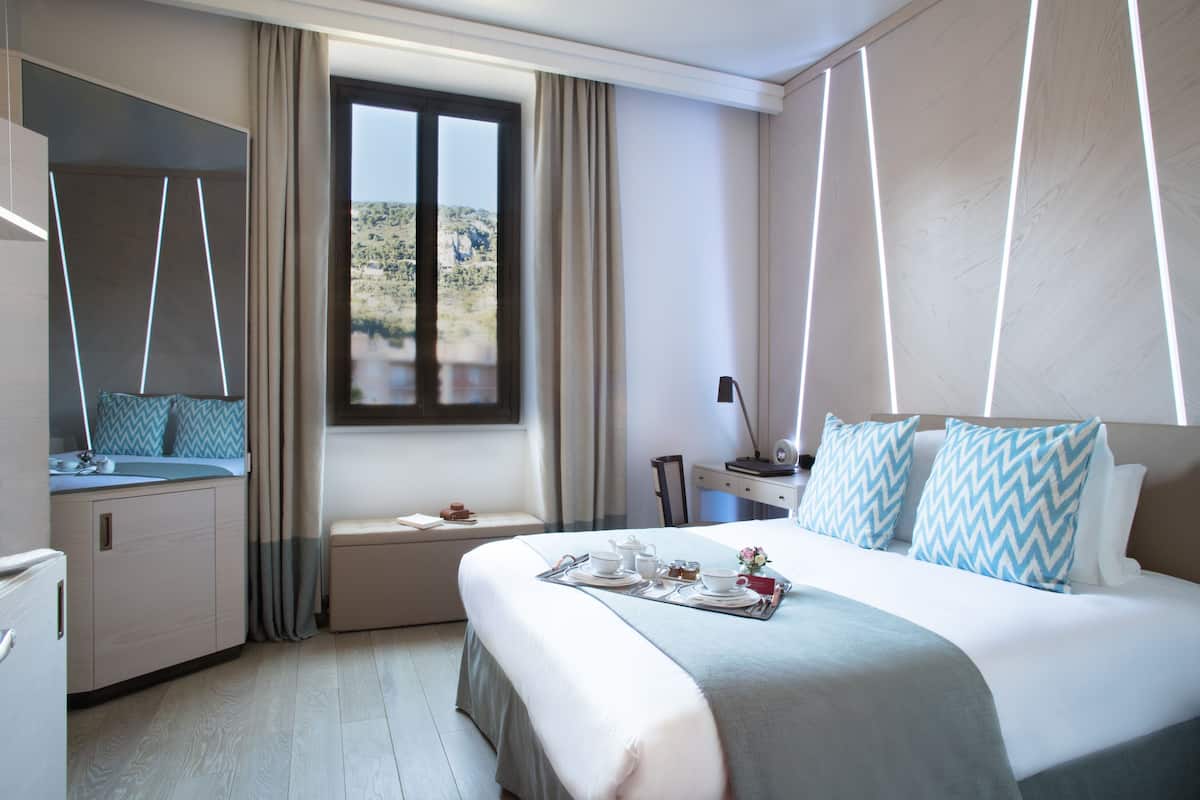 A hotel room with a bed, a window, a desk, and a chair.