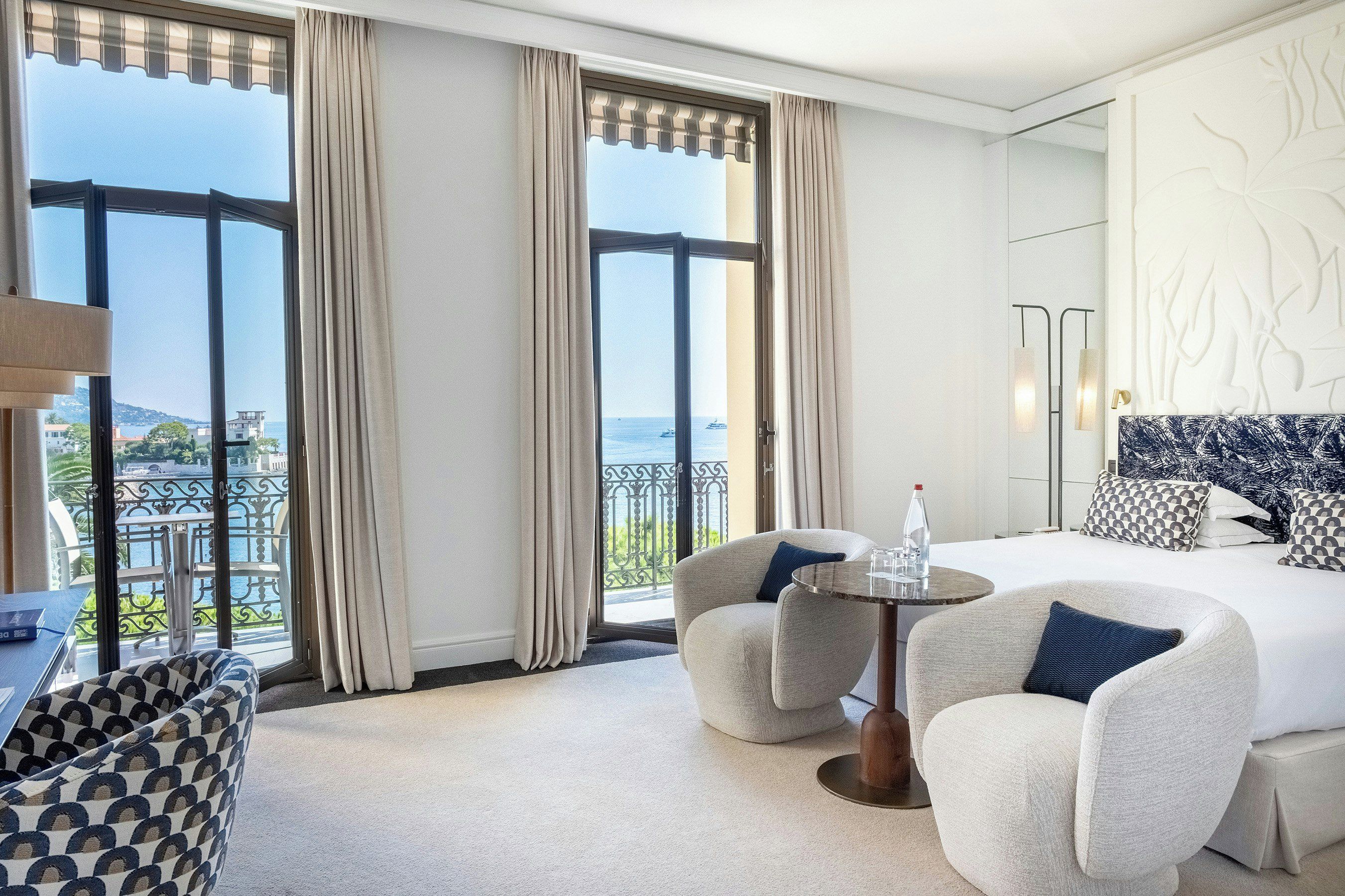 Habitación de hotel con balcón, una cama, dos sillones, una mesita y vista al mar.