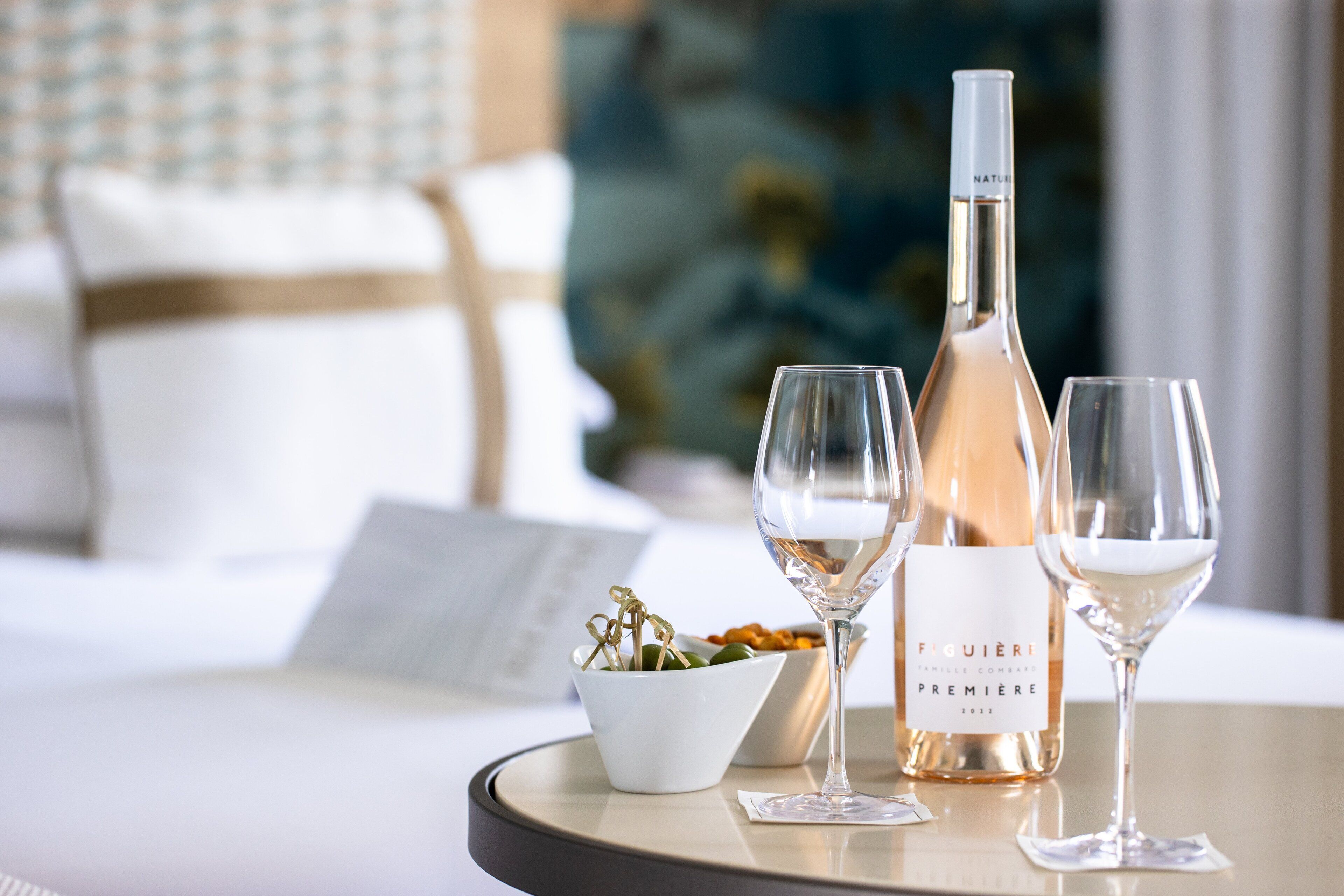 Une table avec une bouteille de vin, deux verres et un saladier de fruits dans une chambre d’hôtel.
