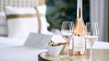 Une table avec une bouteille de vin, deux verres et un saladier de fruits dans une chambre d’hôtel.