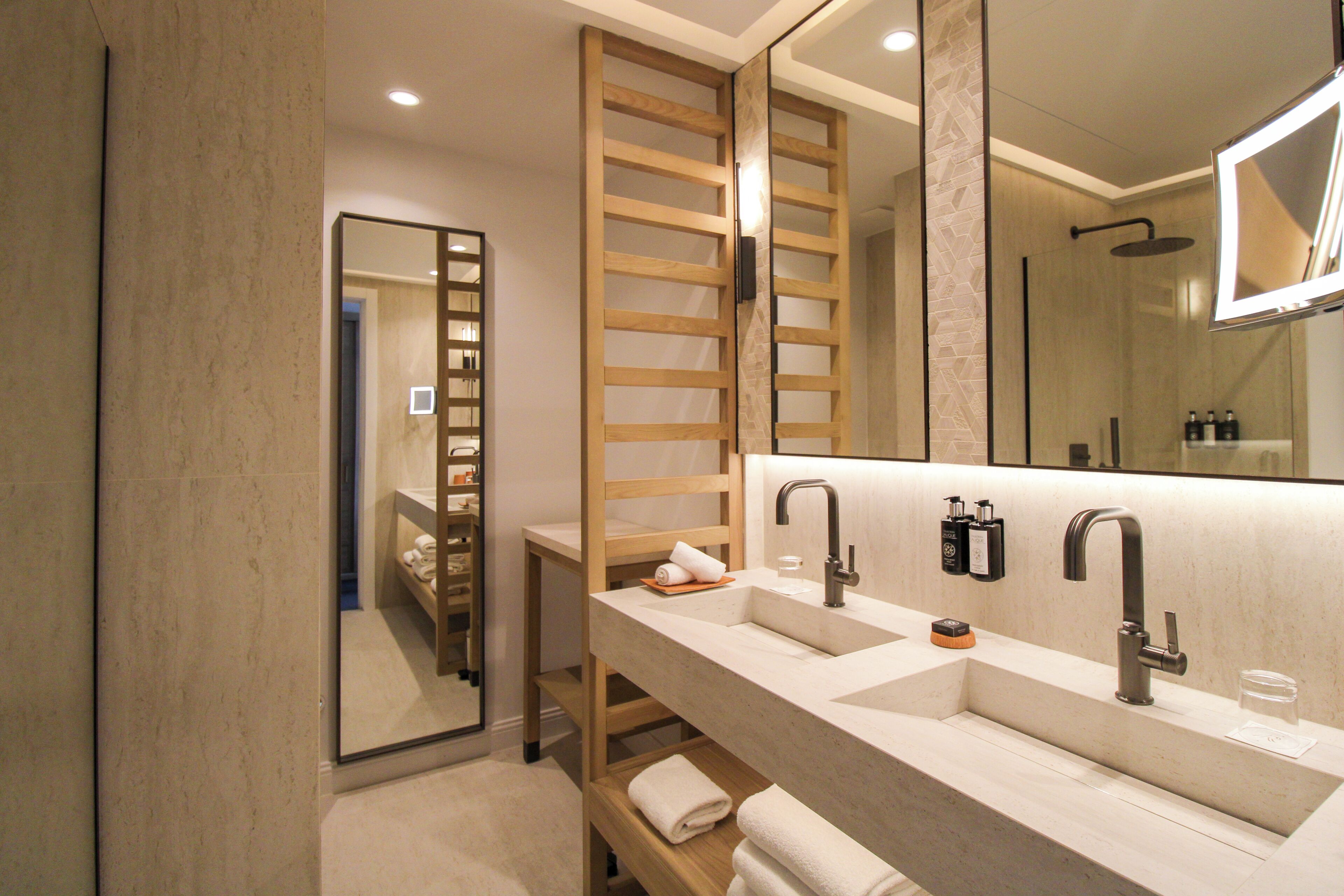 A modern bathroom with a large mirror, two sinks, and a shower area.