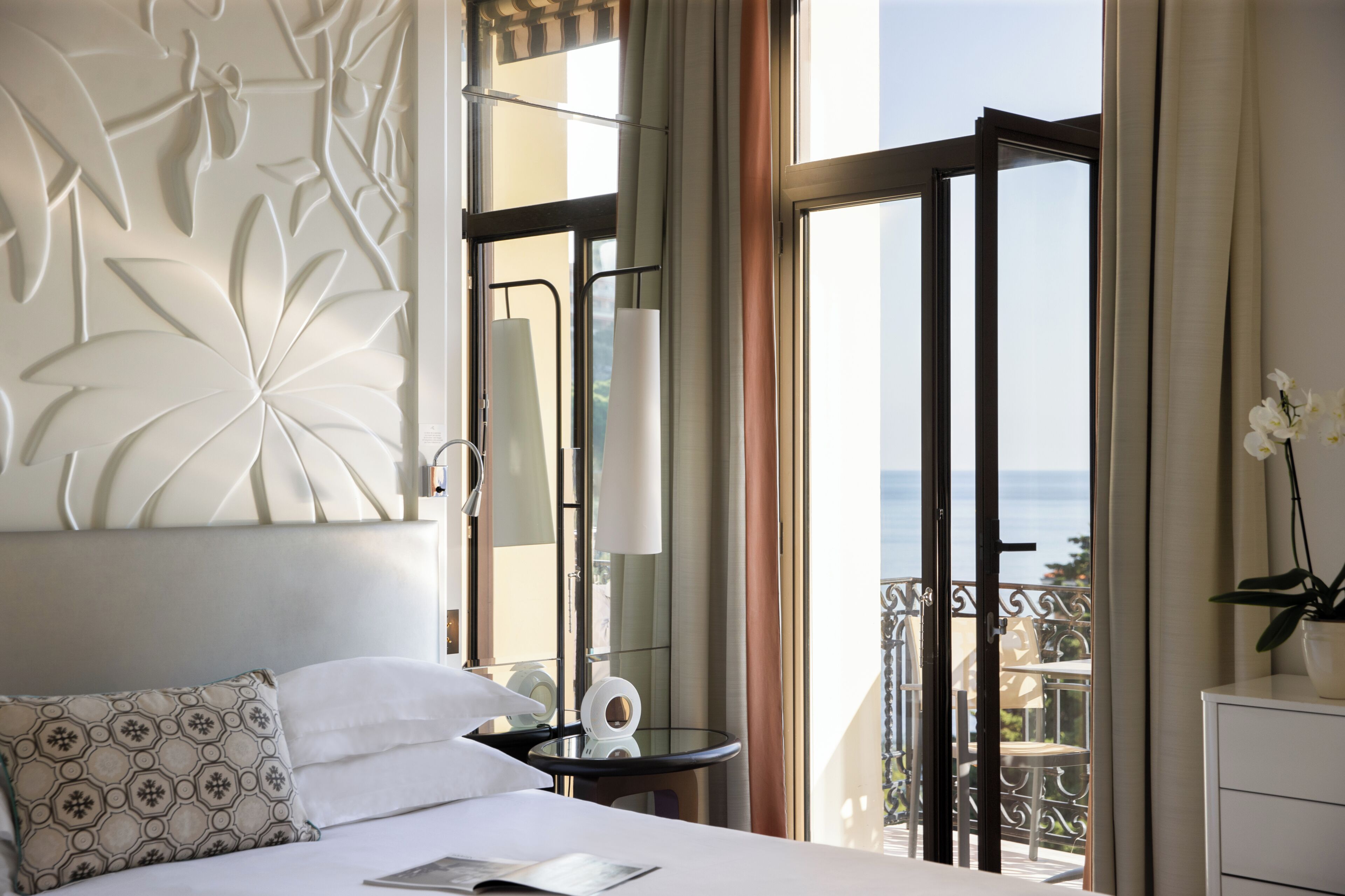 Une chambre d’hôtel comprenant un lit, une petite table, une table de chevet, un panneau décoratif au mur et un balcon avec vue.