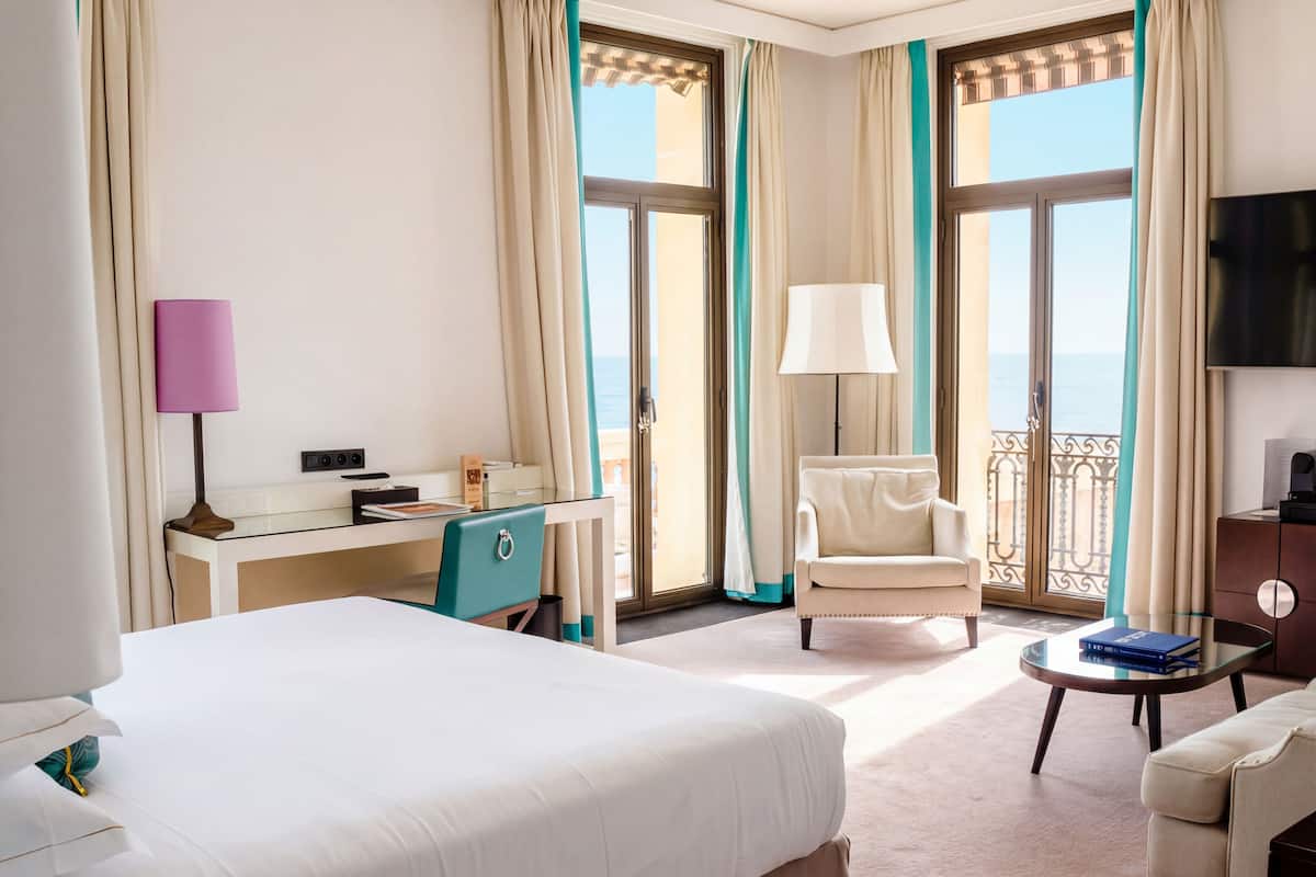 A hotel room with a bed, a desk, a chair, a small table, and a TV.