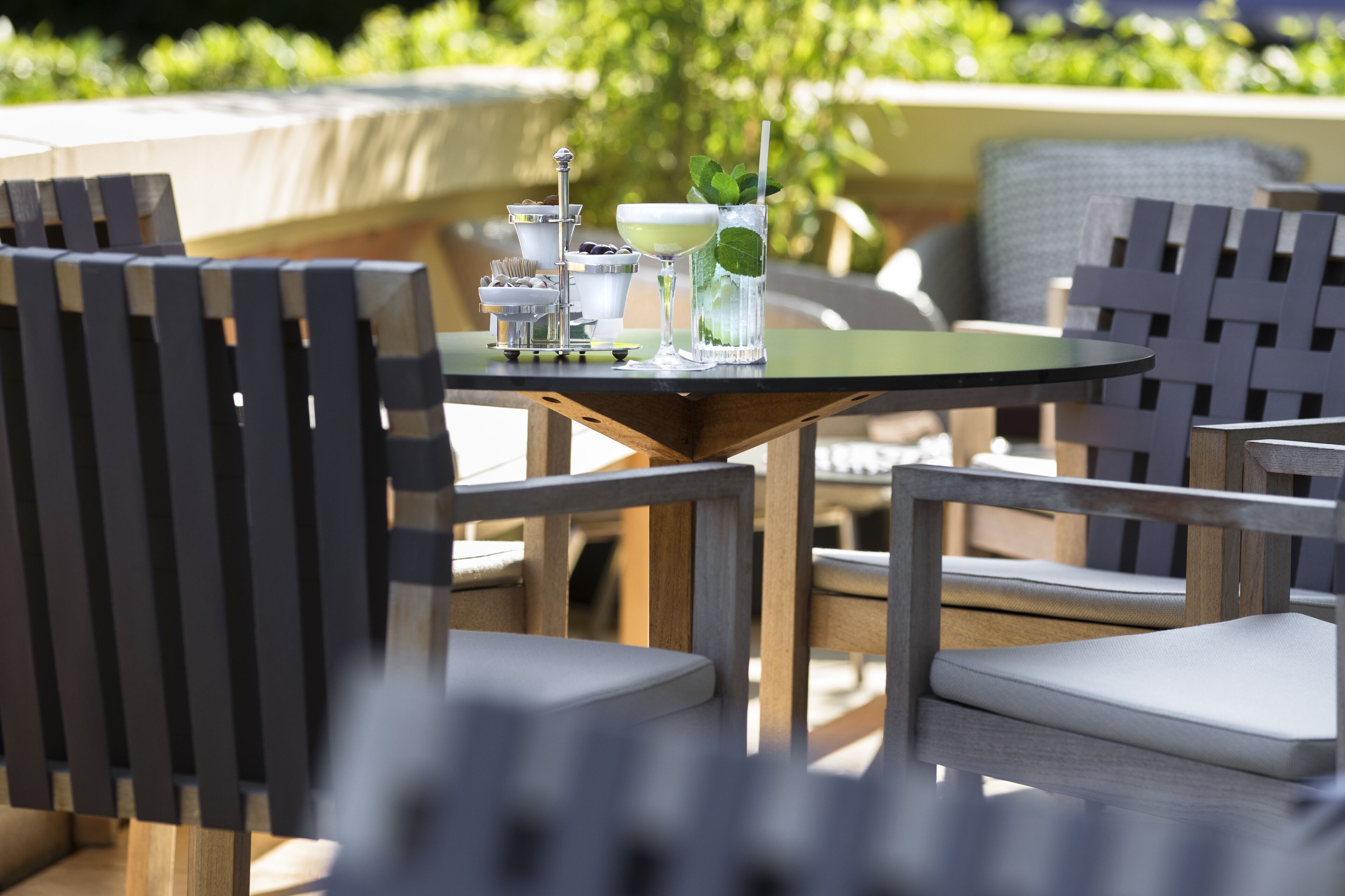 A table with a drink and a small dessert stand, surrounded by chairs with cushions.