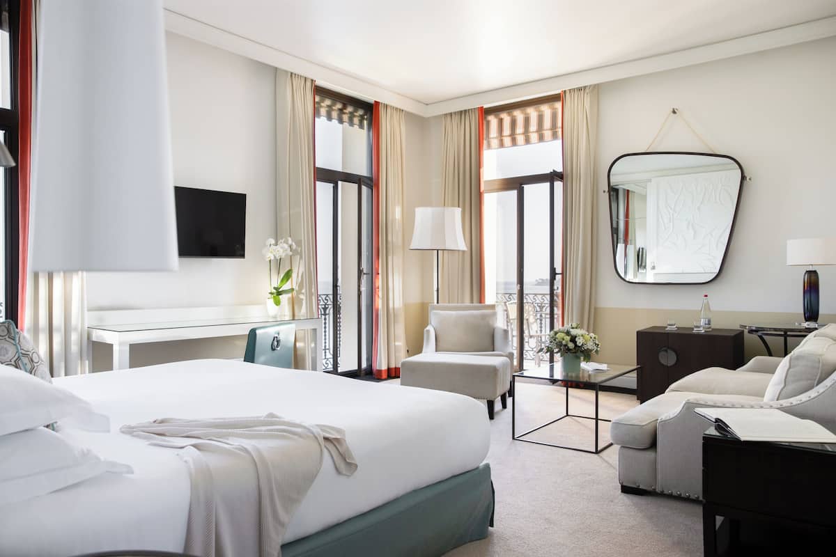 A hotel room with a large bed, a desk, a chair, a sofa, a TV, and a mirror.