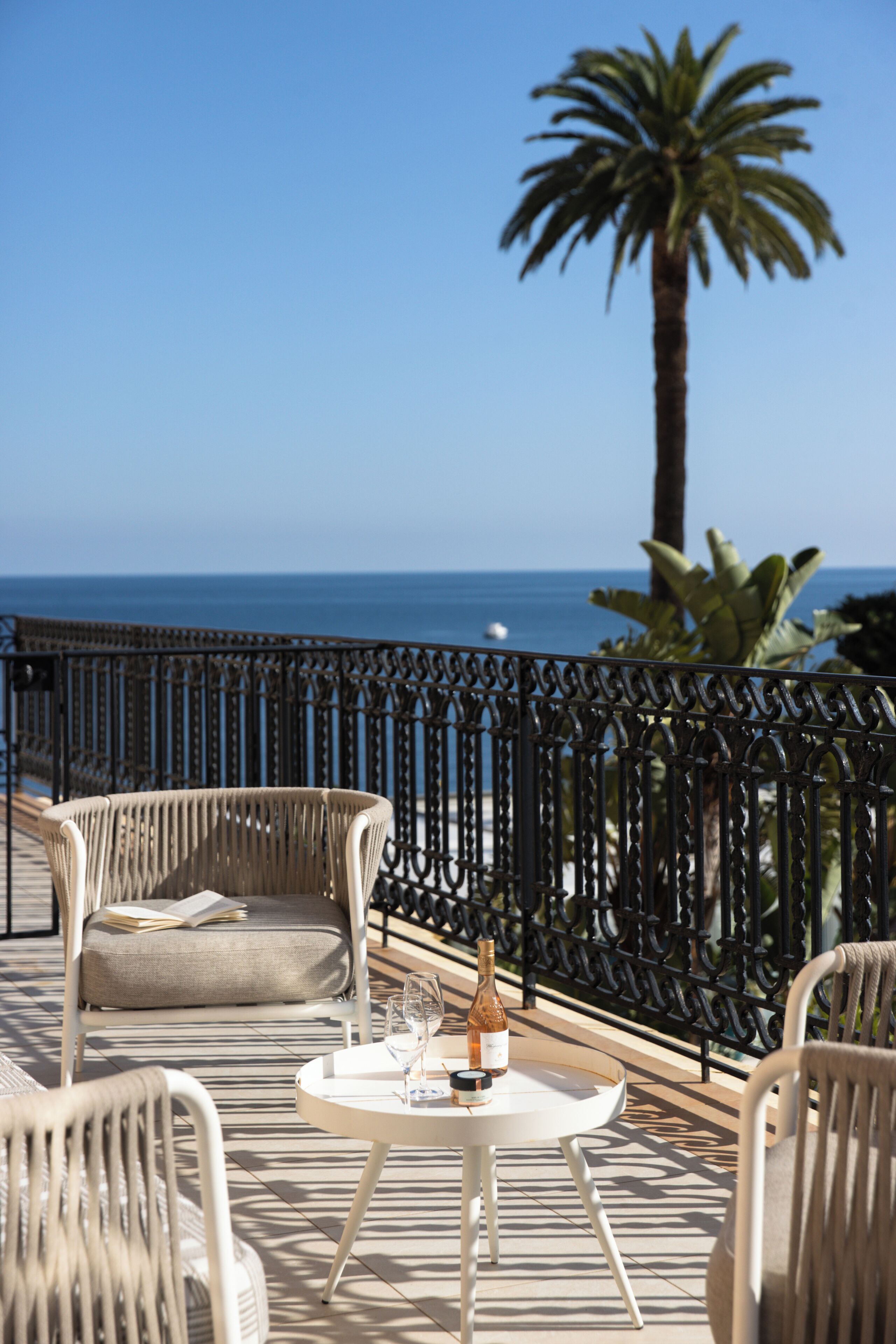 Une terrasse avec des chaises et une table en osier, offrant une vue sur une plage et l’océan.