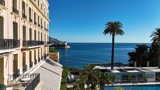 Un hôtel avec une piscine, une vue sur la mer et un palmier.