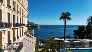 A hotel with a pool, a view of the sea, and a palm tree.