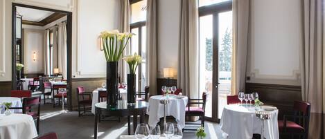 A dining area with round tables, chairs, and a central vase with flowers.
