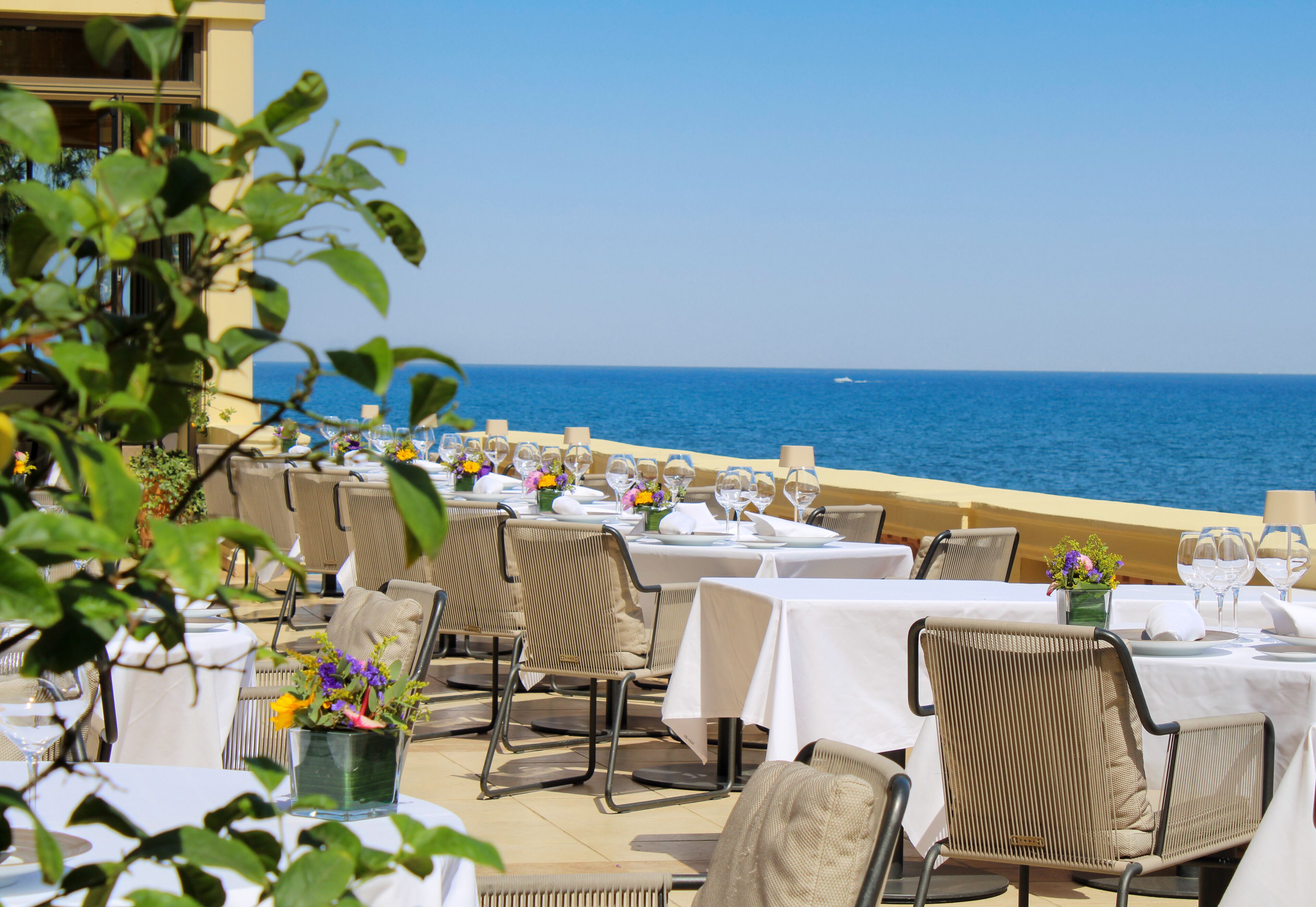 An outdoor dining area with tables set for two, overlooking the sea.