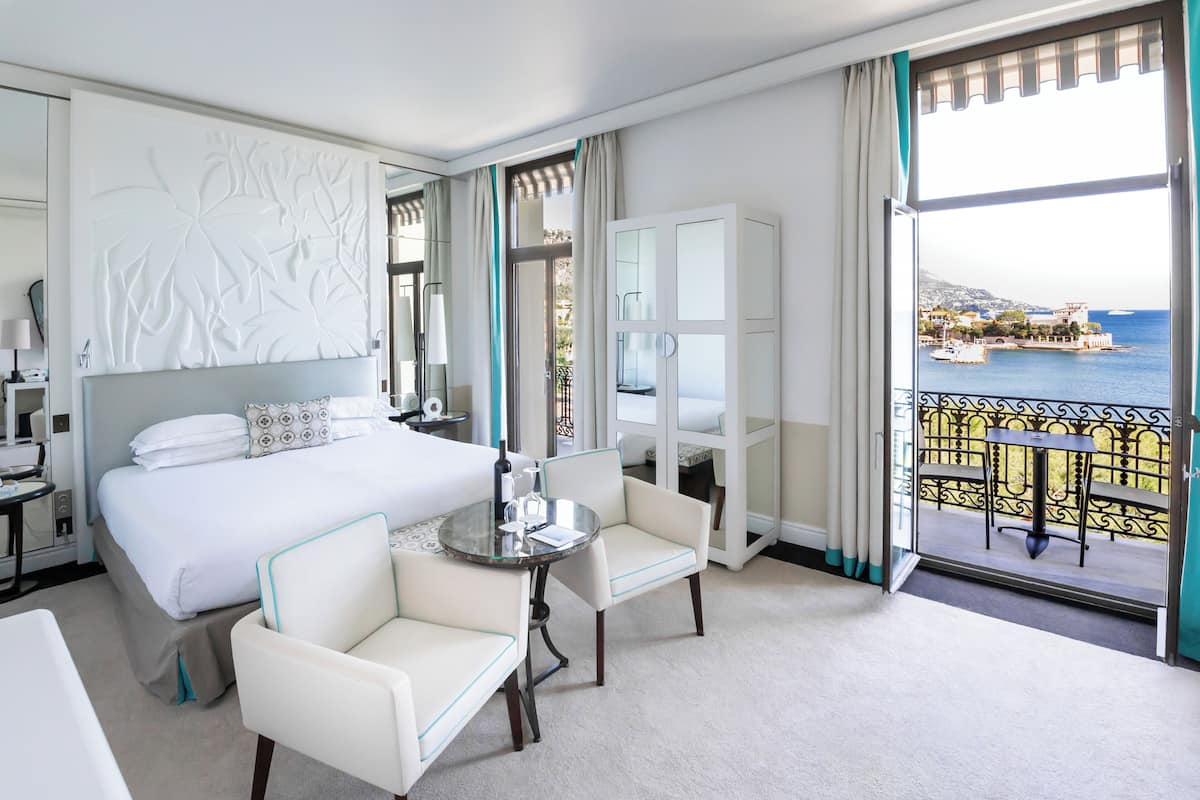 A hotel room with a bed, a desk, a chair, a balcony with a view of the sea.