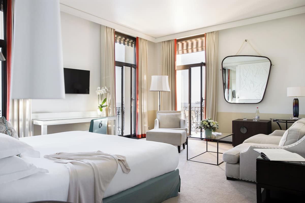 A hotel room with a large bed, a desk, a chair, a sofa, a small table, and a mirror.