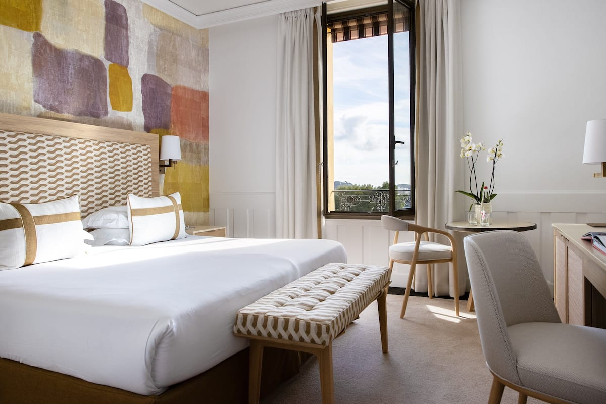 A hotel room with a large bed, a bench, a desk, and a chair.