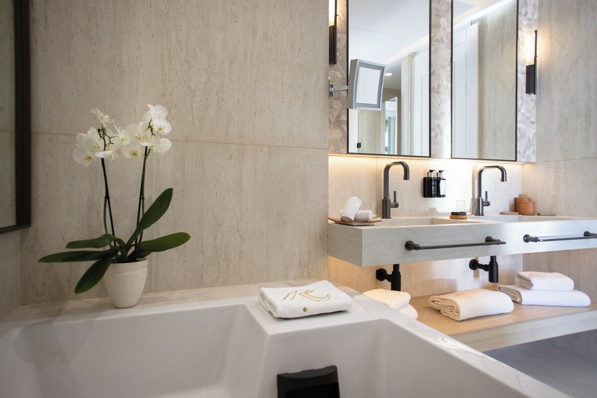 A modern bathroom with a large bathtub, a countertop with a potted orchid, and a mirror above the sink.