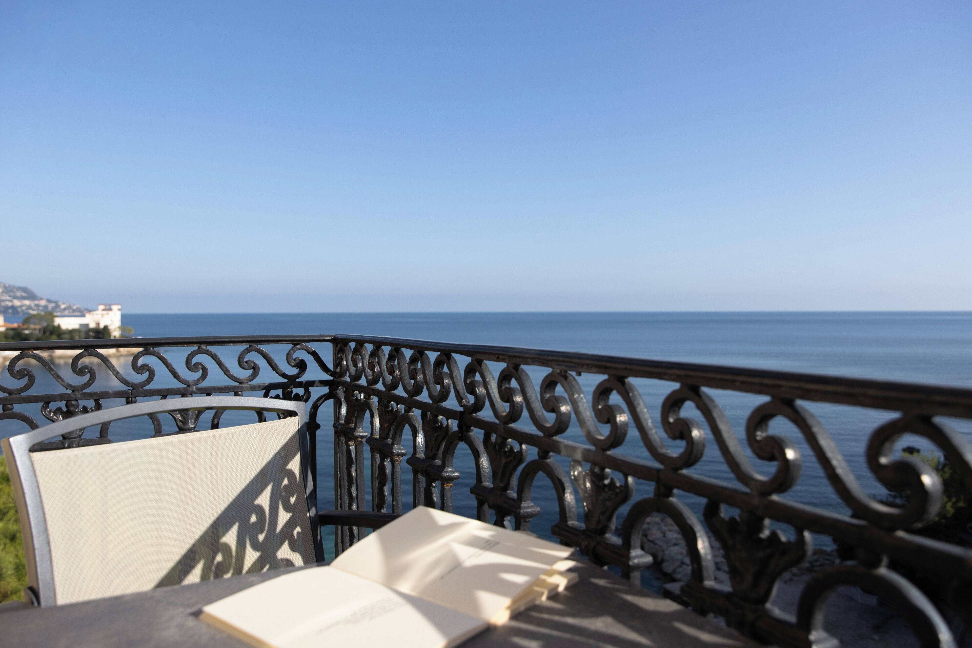 A balcony with a view of the sea, a chair, and an open book.