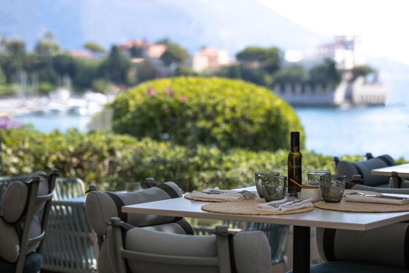 A dining table set with a bottle, glasses, and a placemat, overlooking a marina with boats and greenery.