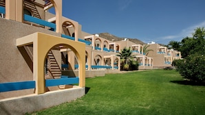 A row of resort-style buildings with arched balconies and a well-maintained lawn.