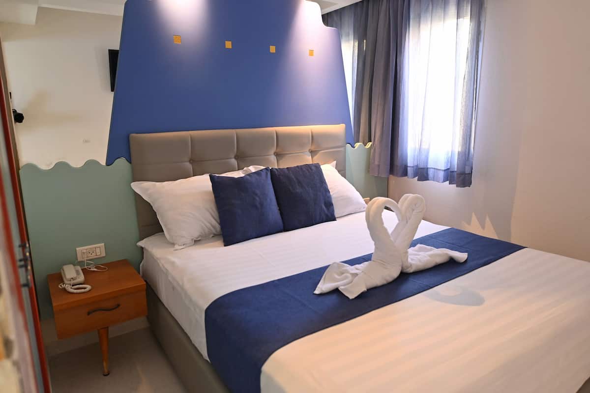 Een hotelkamer met een bed, een nachtkastje met een telefoon en een raam met gordijnen.