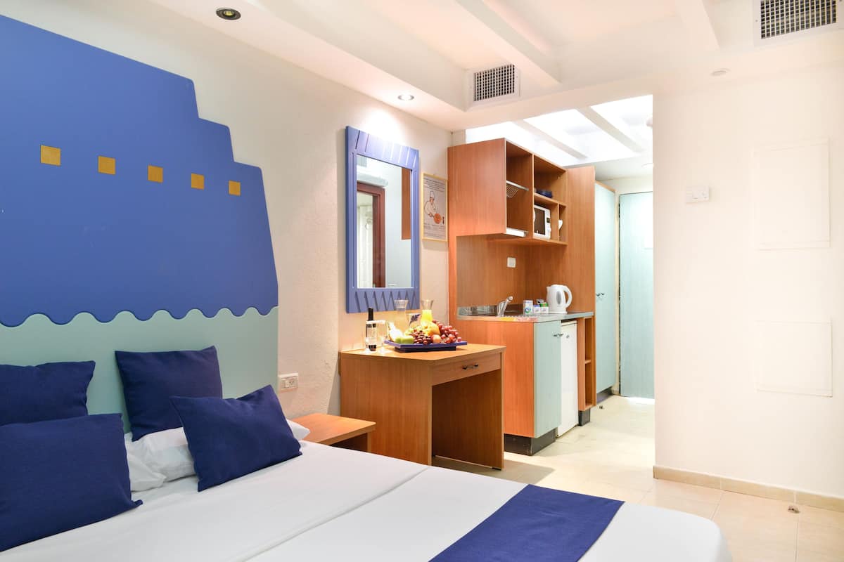 Een hotelkamer met een bed, een bureau met een fruitschaal, een spiegel en een kitchenette.