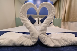 Uma cama com arranjo de toalha em formato de coração sobre um lençol azul.