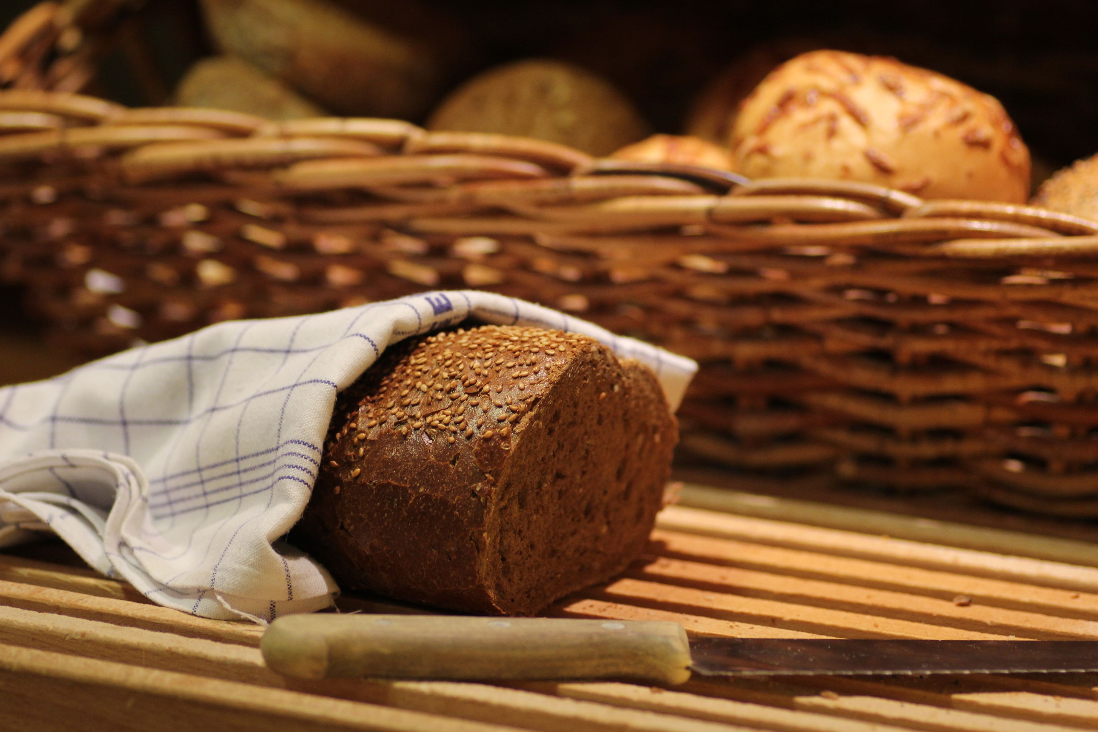 A loaf of bread with sesame seeds on a wooden surface, accompanied by a knife and a cloth.