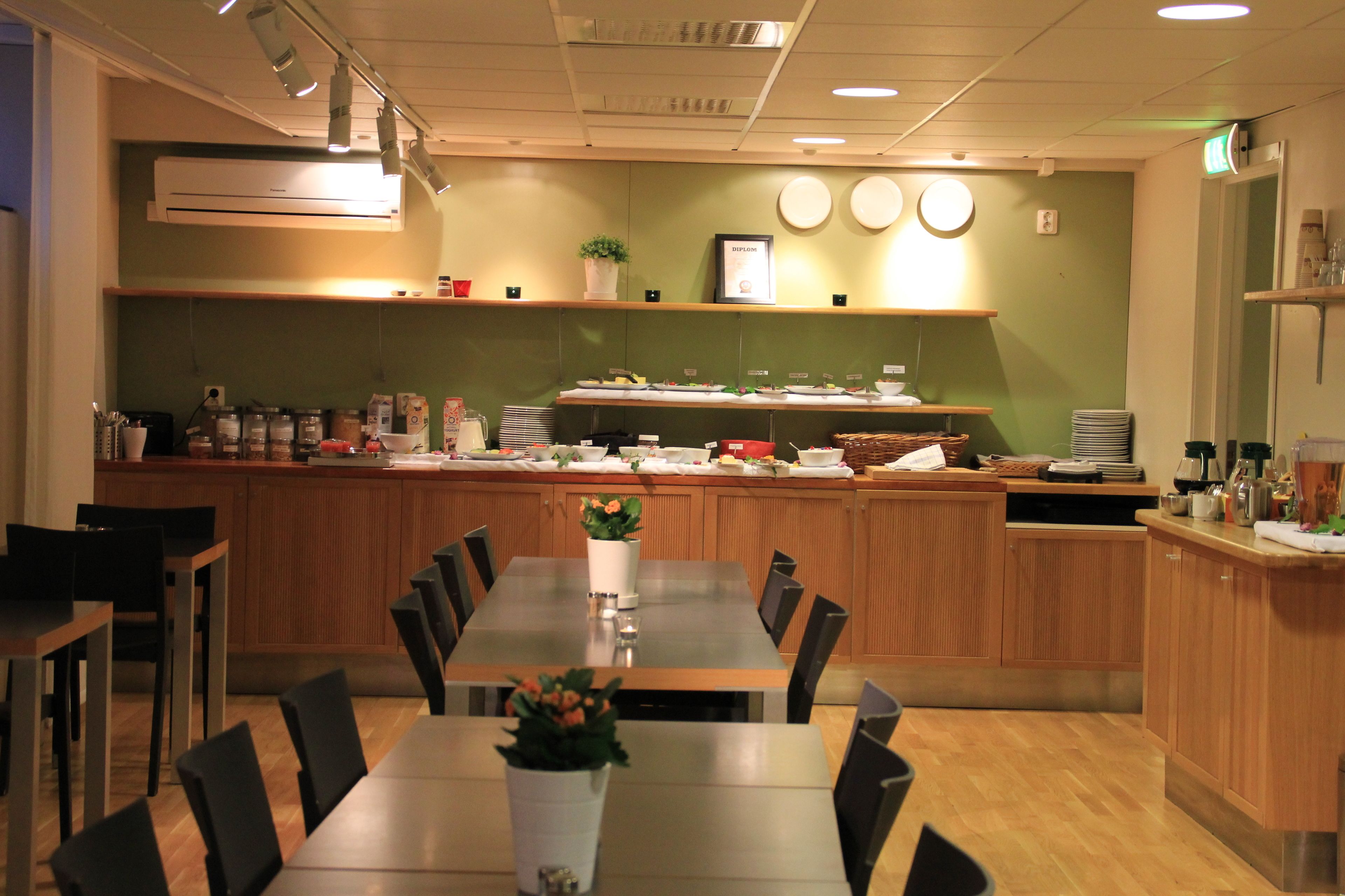 Ein Restaurant mit einer langen Theke, mehreren Tischen und Stühlen. Über der Theke befinden sich Regale mit verschiedenen Gegenständen, und eine Wandklimaanlage ist angebracht.